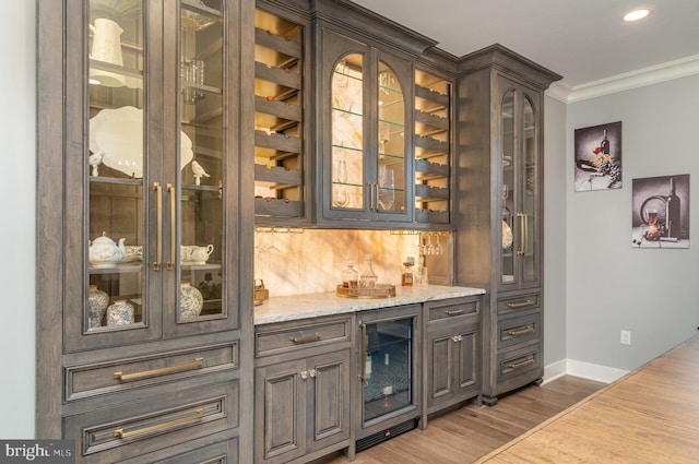 bar with light stone counters, ornamental molding, dark brown cabinets, hardwood / wood-style flooring, and wine cooler