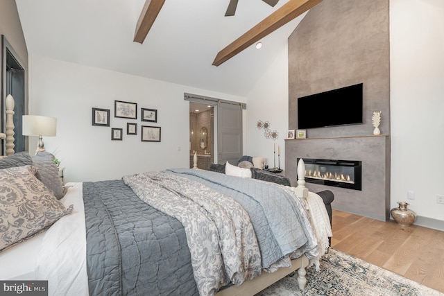 bedroom featuring ceiling fan, a large fireplace, a barn door, lofted ceiling with beams, and hardwood / wood-style floors