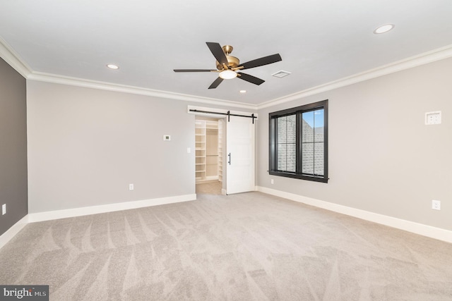 unfurnished bedroom with a walk in closet, light colored carpet, ceiling fan, crown molding, and a barn door