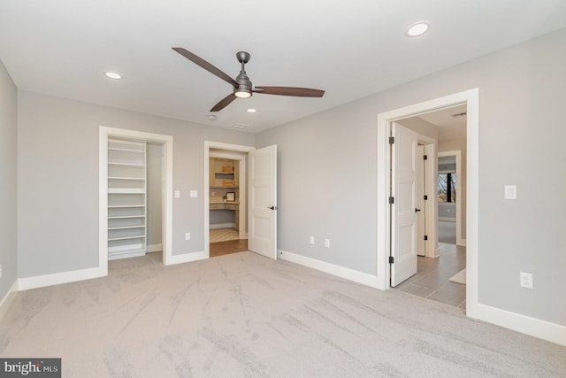 unfurnished bedroom featuring a spacious closet, a closet, ceiling fan, and light carpet