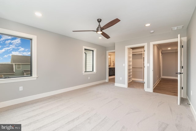 unfurnished bedroom with a walk in closet, light colored carpet, ceiling fan, multiple windows, and a closet