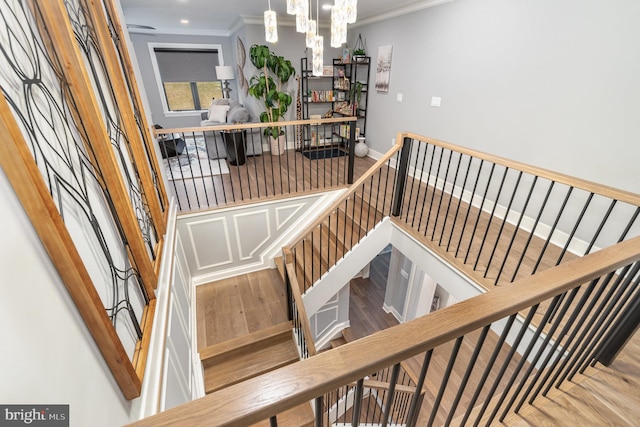 stairway featuring hardwood / wood-style flooring, ornamental molding, and a notable chandelier