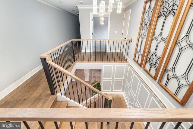 stairway featuring a chandelier, wood-type flooring, and ornamental molding