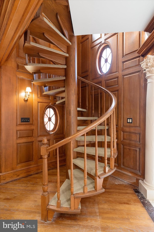 staircase with ornate columns, wooden walls, and wood-type flooring