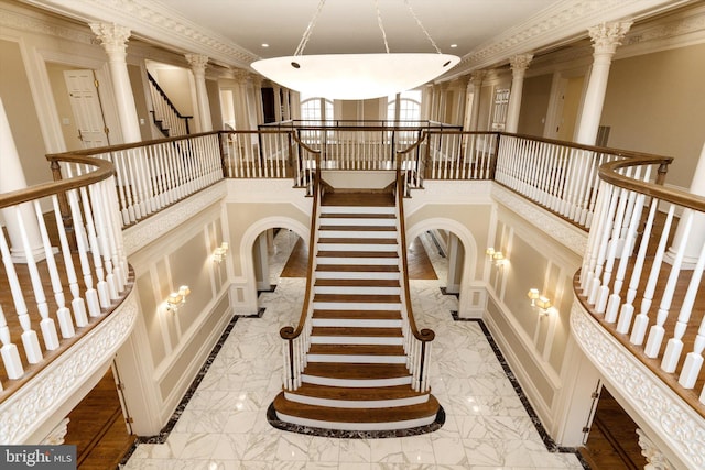 stairs with a towering ceiling, decorative columns, and crown molding