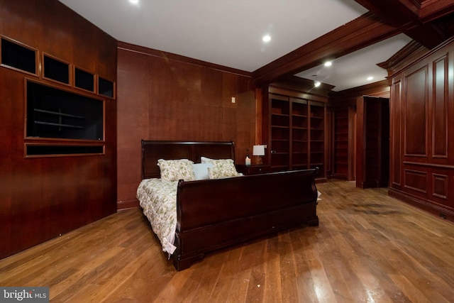 bedroom with beamed ceiling, hardwood / wood-style floors, ornamental molding, and wood walls