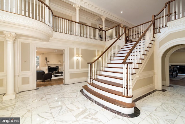 stairs with ornamental molding, a high ceiling, and ornate columns