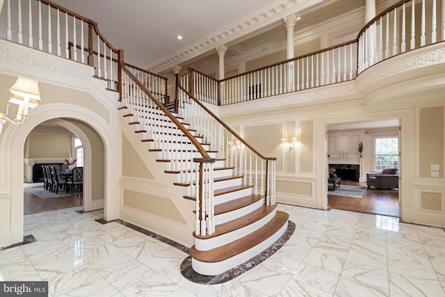 stairs with a high end fireplace, crown molding, hardwood / wood-style floors, and a towering ceiling