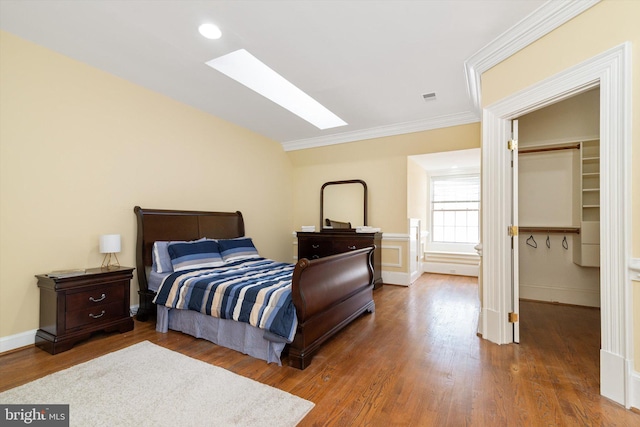 bedroom with dark hardwood / wood-style flooring, a skylight, crown molding, a spacious closet, and a closet