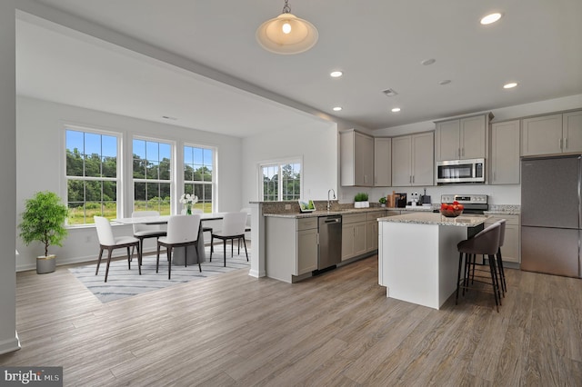 kitchen with light stone counters, gray cabinetry, stainless steel appliances, pendant lighting, and light hardwood / wood-style floors