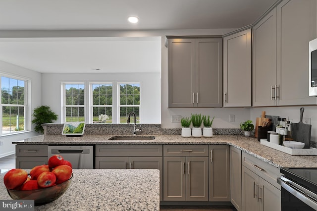 kitchen featuring light stone counters, sink, stainless steel appliances, and a wealth of natural light