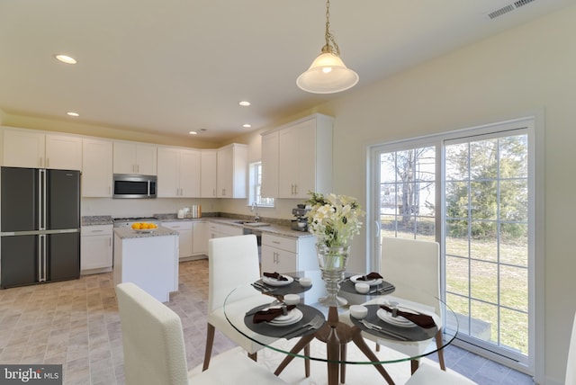 kitchen with white cabinetry, black refrigerator, light stone countertops, and decorative light fixtures