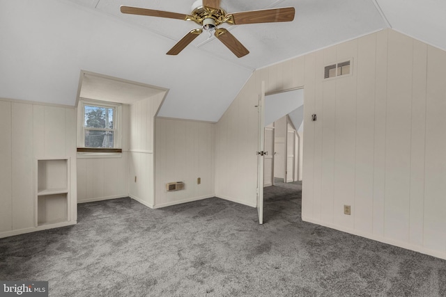 bonus room with lofted ceiling, built in shelves, ceiling fan, and dark colored carpet