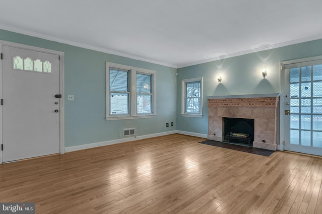 unfurnished living room with a tile fireplace, ornamental molding, and light hardwood / wood-style floors