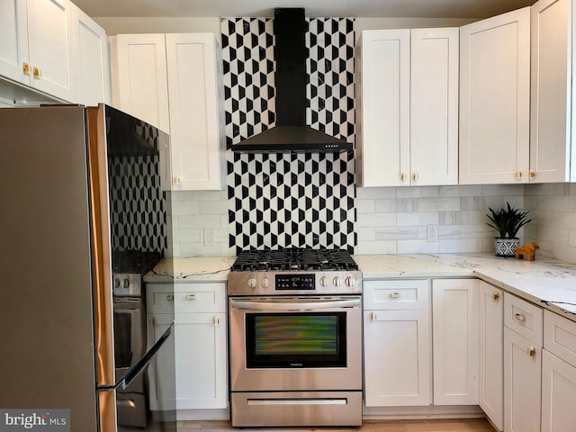 kitchen with white cabinets, appliances with stainless steel finishes, wall chimney exhaust hood, and light stone counters