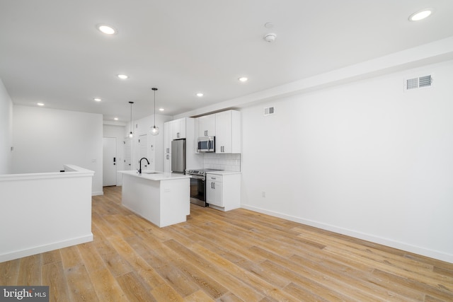 kitchen with appliances with stainless steel finishes, hanging light fixtures, light hardwood / wood-style floors, and an island with sink