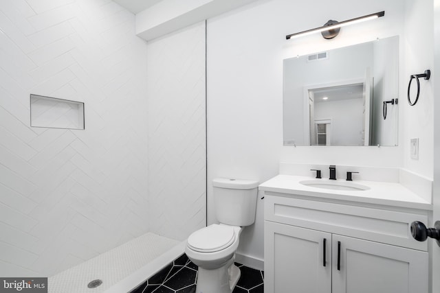 bathroom featuring tile flooring, toilet, a tile shower, and vanity with extensive cabinet space