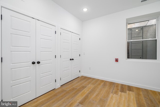 unfurnished bedroom featuring multiple closets and light wood-type flooring