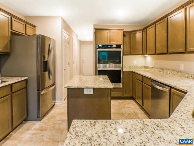 kitchen with appliances with stainless steel finishes, a kitchen island, light stone counters, and light tile floors