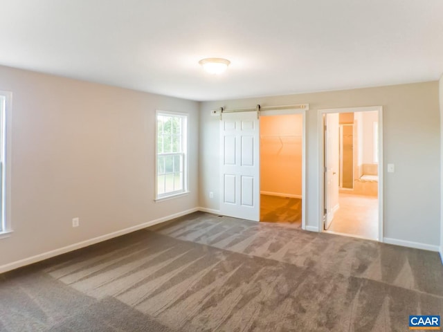 unfurnished bedroom with light carpet, a barn door, a spacious closet, and a closet