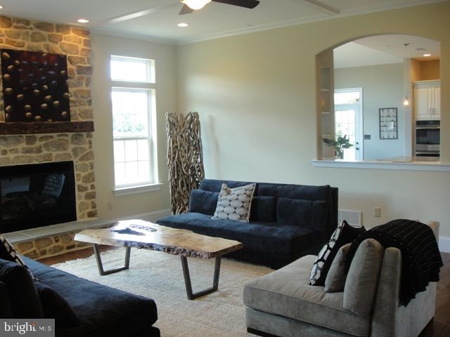 living room featuring ceiling fan, ornamental molding, a healthy amount of sunlight, and a stone fireplace