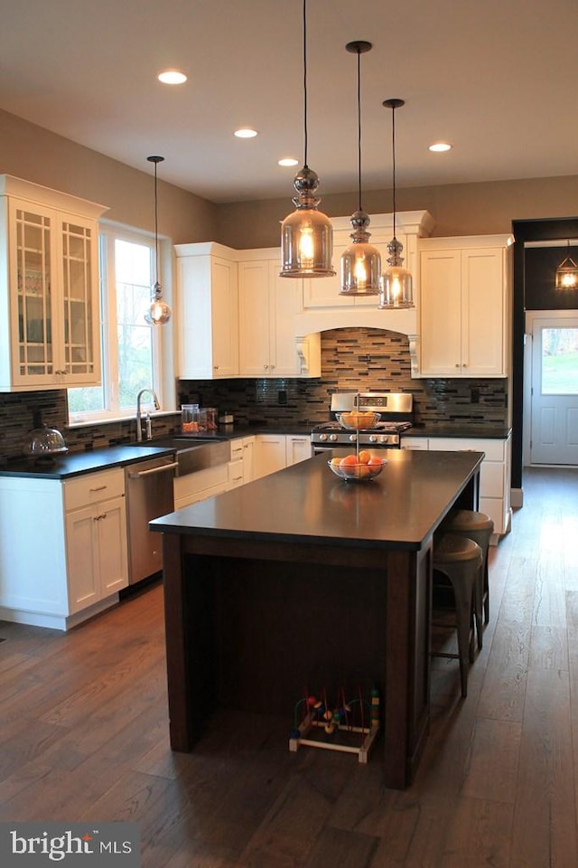 kitchen with a center island, decorative light fixtures, white cabinetry, appliances with stainless steel finishes, and dark hardwood / wood-style flooring