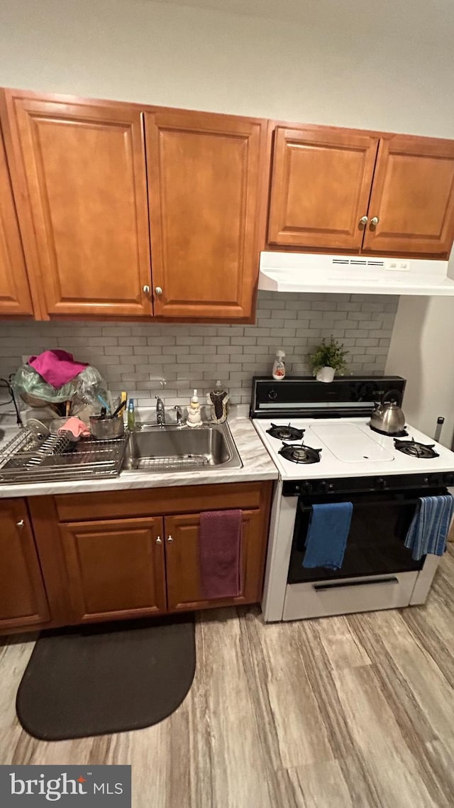 kitchen with light wood-type flooring, white electric stove, backsplash, and sink