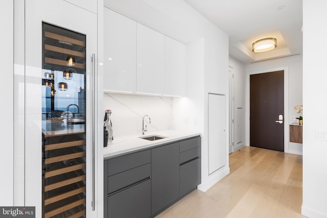 kitchen featuring a raised ceiling, sink, white cabinetry, gray cabinets, and light wood-type flooring