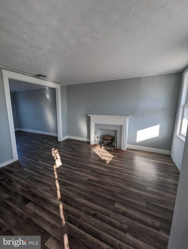 unfurnished living room with a brick fireplace, dark hardwood / wood-style floors, and a textured ceiling