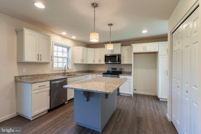 kitchen with decorative light fixtures, appliances with stainless steel finishes, a kitchen island, light stone countertops, and white cabinets