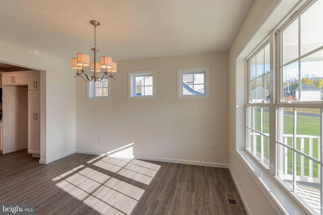 spare room featuring an inviting chandelier, a healthy amount of sunlight, and dark hardwood / wood-style flooring