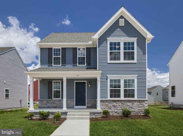 view of front of house featuring covered porch, stone siding, a shingled roof, and a front yard