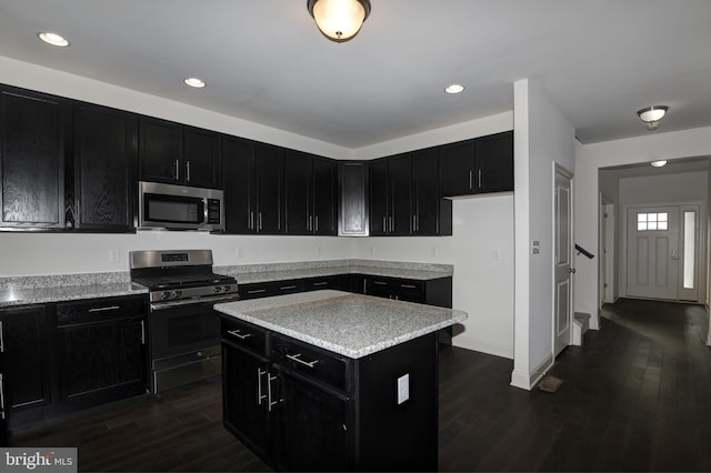 kitchen with appliances with stainless steel finishes, light stone countertops, a center island, and dark hardwood / wood-style floors