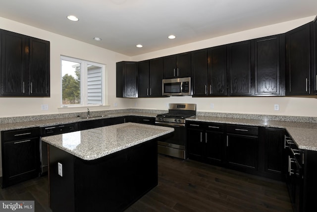 kitchen featuring appliances with stainless steel finishes, light stone counters, a kitchen island, sink, and dark hardwood / wood-style floors