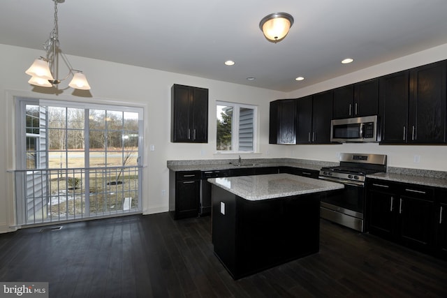 kitchen with decorative light fixtures, an inviting chandelier, appliances with stainless steel finishes, a center island, and dark hardwood / wood-style flooring