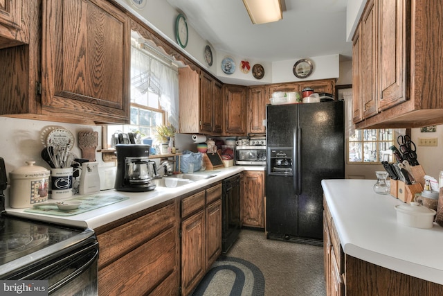 kitchen with sink, dark colored carpet, black appliances, and a wealth of natural light