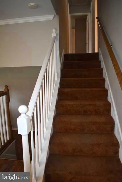 stairs featuring crown molding and dark wood-type flooring