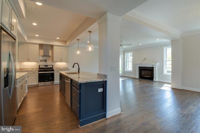 kitchen with white cabinetry, stainless steel appliances, hardwood / wood-style floors, wall chimney exhaust hood, and ceiling fan