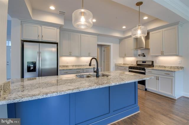 kitchen featuring sink, a raised ceiling, appliances with stainless steel finishes, wall chimney range hood, and decorative light fixtures