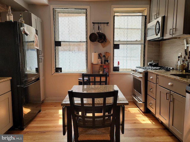 kitchen featuring tasteful backsplash, light hardwood / wood-style floors, appliances with stainless steel finishes, and light stone counters