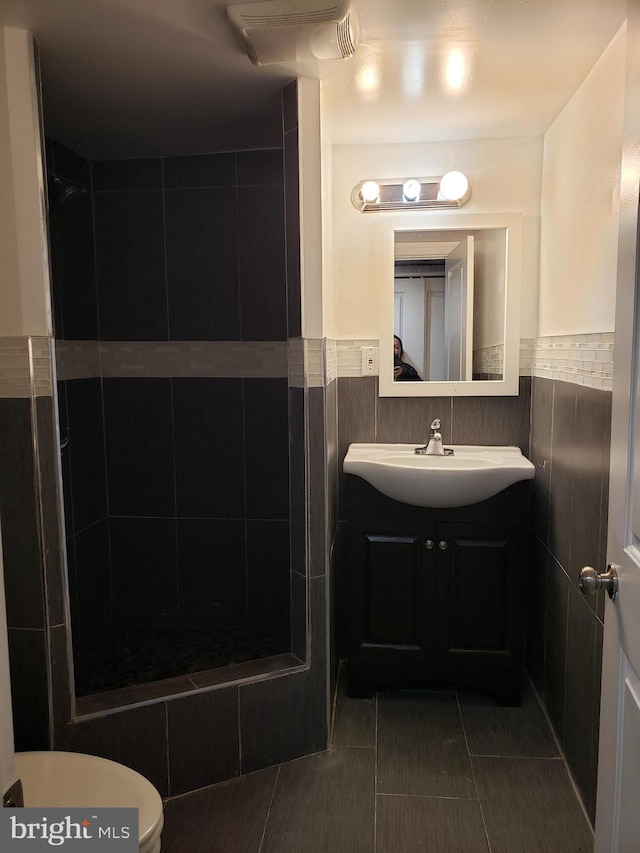 bathroom featuring toilet, vanity, tiled shower, tile walls, and backsplash