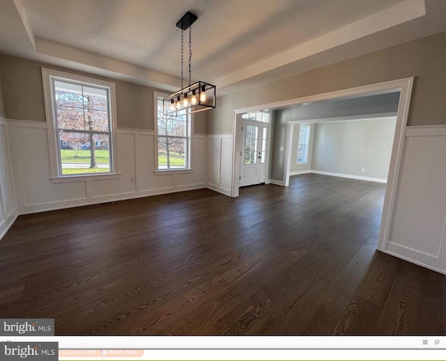 unfurnished room featuring a tray ceiling, a notable chandelier, and dark hardwood / wood-style floors