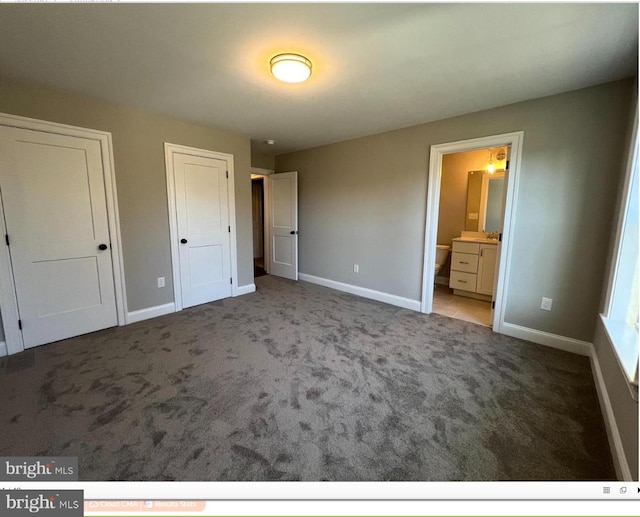 unfurnished bedroom featuring ensuite bath and dark carpet