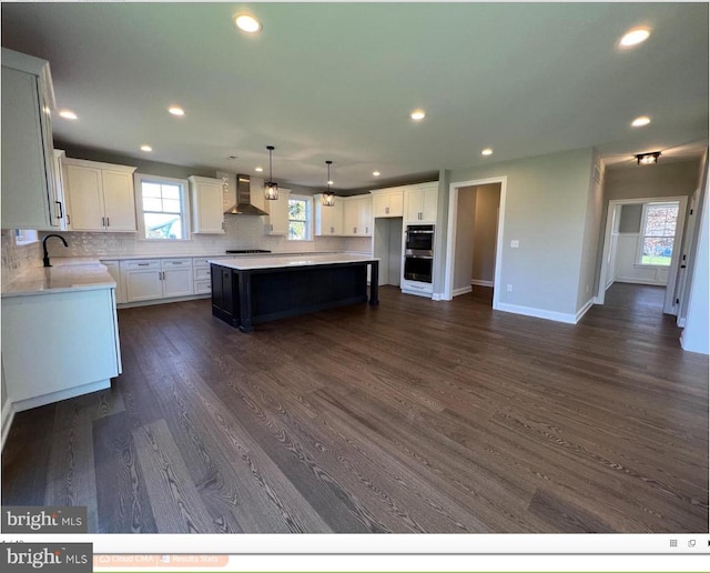 kitchen featuring white cabinetry, dark wood-type flooring, sink, a kitchen island, and wall chimney exhaust hood