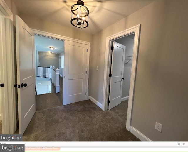 hall featuring a notable chandelier and dark colored carpet