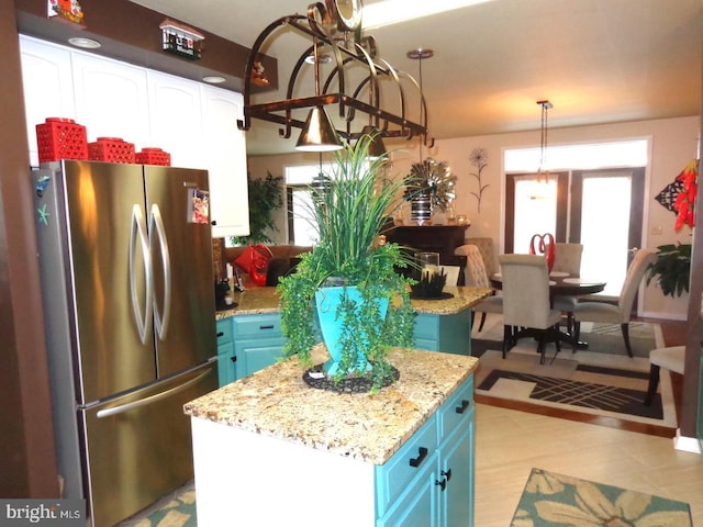 kitchen with decorative light fixtures, stainless steel refrigerator, light stone counters, a kitchen island, and blue cabinetry