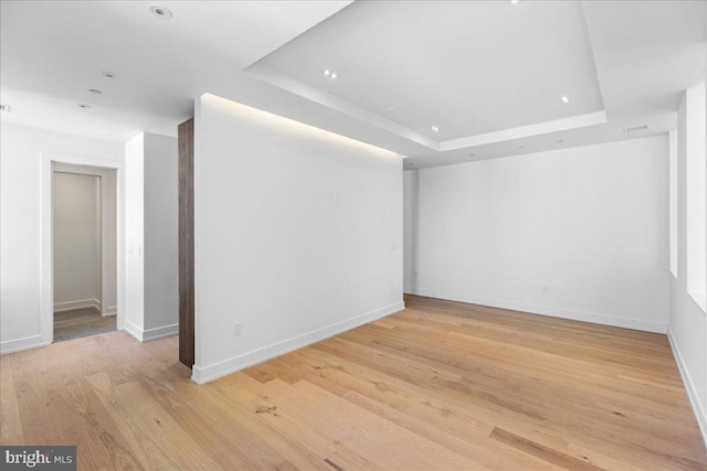 spare room featuring light wood-type flooring and a raised ceiling