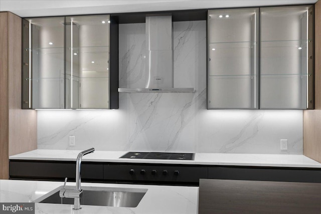 kitchen with tasteful backsplash, black stovetop, wall chimney range hood, and sink