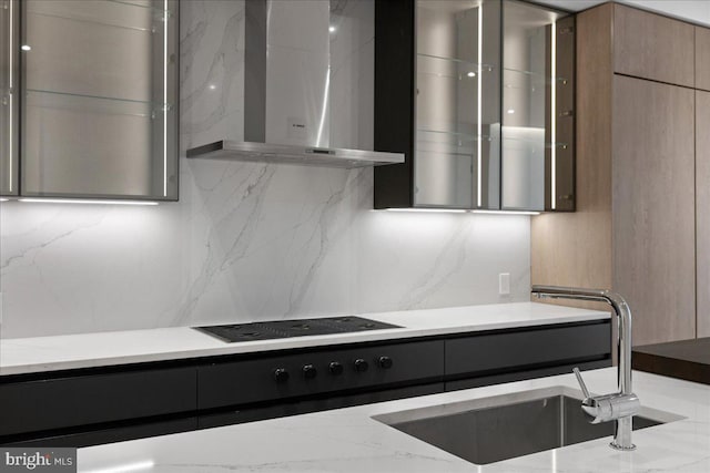 kitchen featuring black electric stovetop, wall chimney exhaust hood, light stone counters, and sink