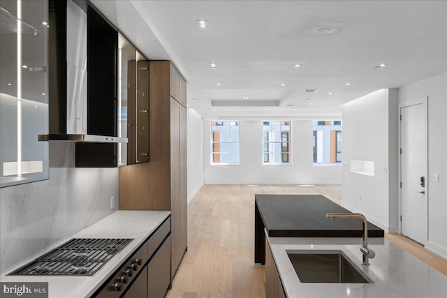 kitchen featuring wall chimney exhaust hood, light hardwood / wood-style floors, sink, and a tray ceiling